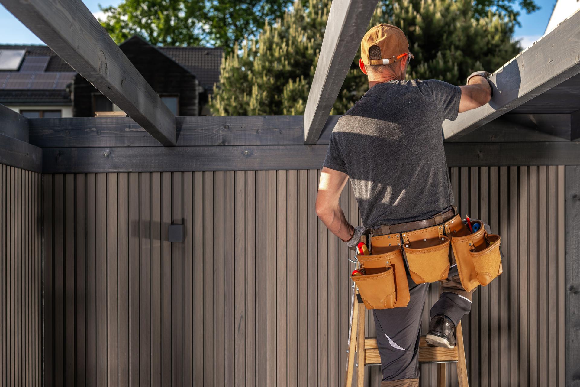Construction Worker Repairing Wooden Beams in a Sunny Backyard During Afternoon Hours